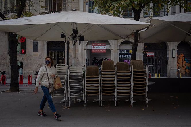 Una mujer pasa junto a la terraza recogida de un bar cerrado (DAVID ZORRAKINO - EUROPA PRESS)