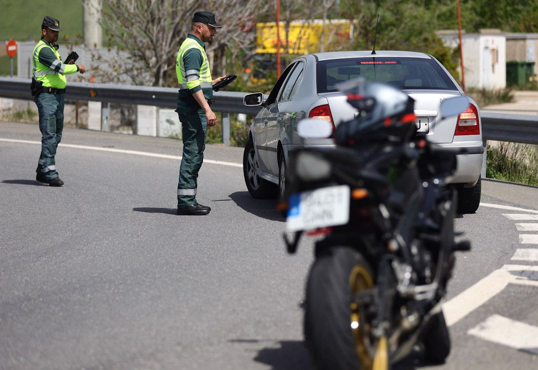 Foto de una motocicleta. Detrás, un agente de la Guardia Civil pide documentación a un conductor en un control de tráfico (EDUARDO PARRA - EUROPA PRESS)